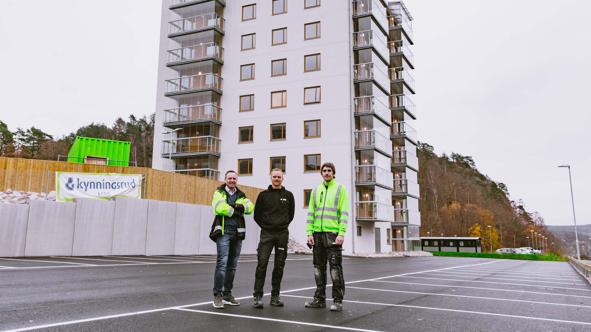 Tre män i arbetskläder framför en bostadsblock